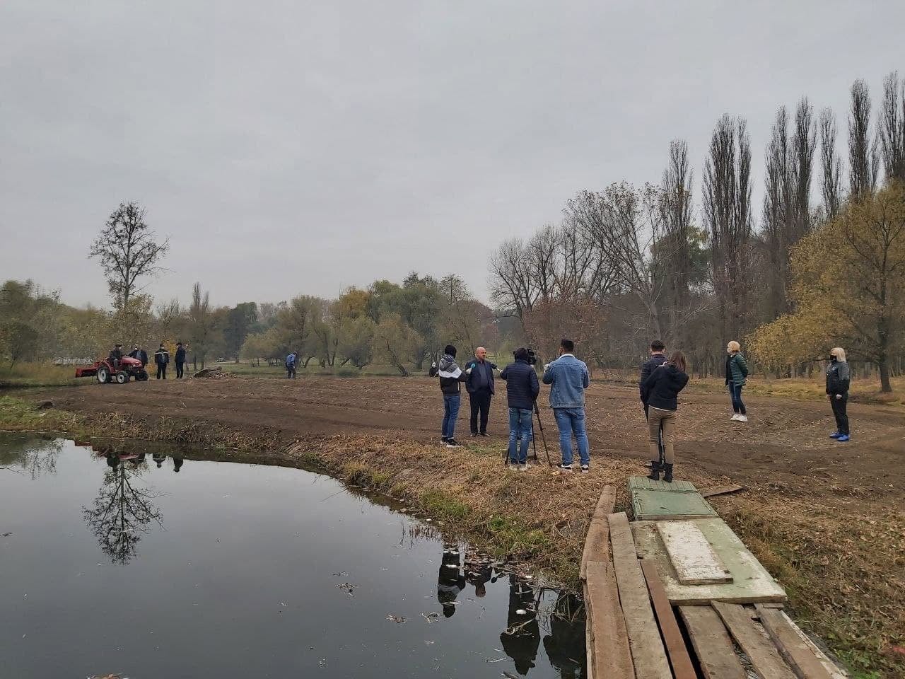 People walking along the shore of a pond surrounded by bare autumn trees