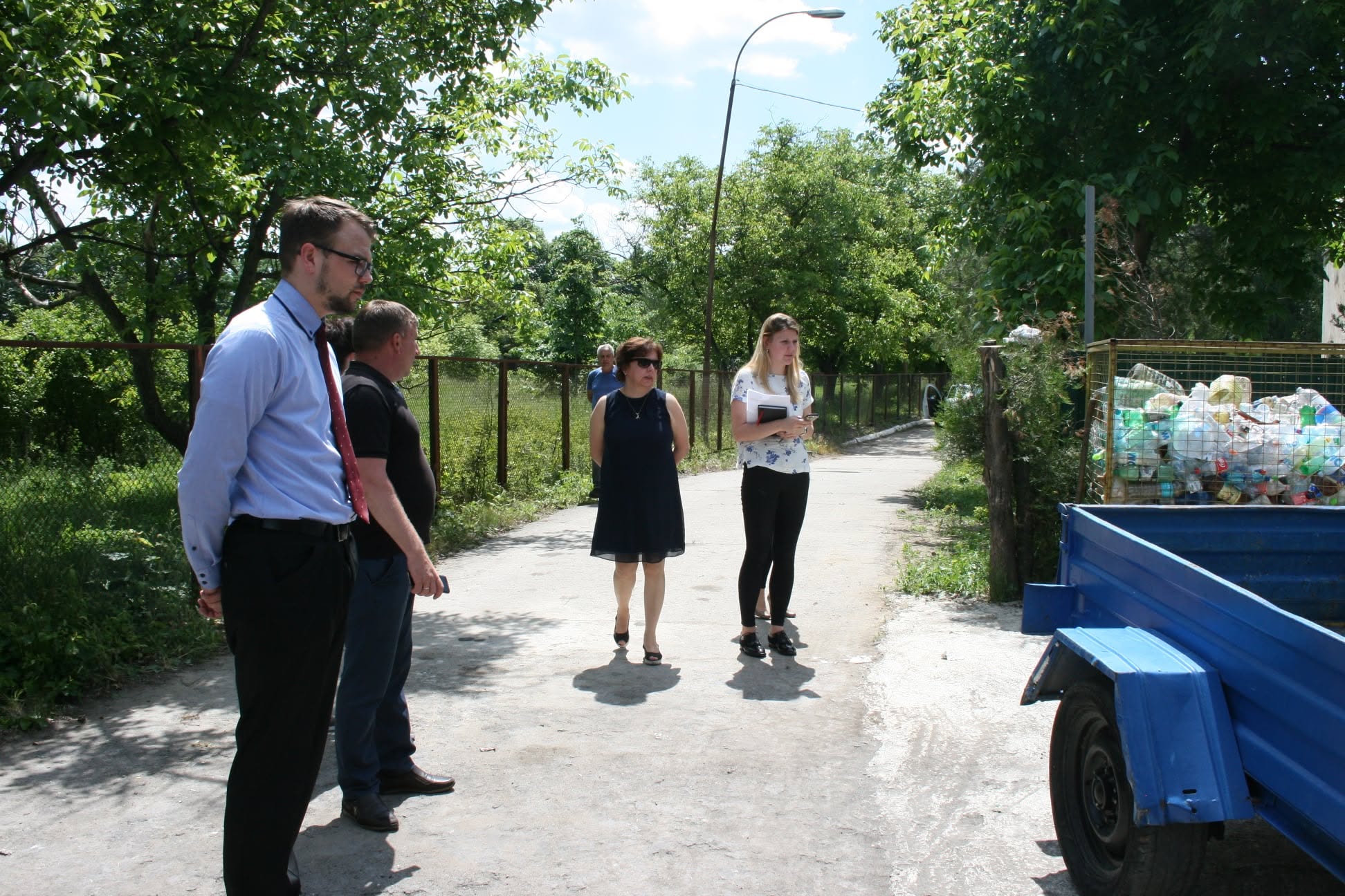 A group of people talking on a tree-lined path near a green area